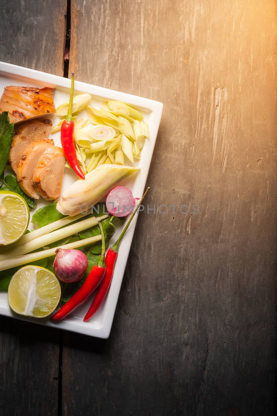 Ingredients set for Thai spicy soup (Tom-yum) include lemon, galangal, red chili, red onion, lemongrass, and kaffir lime leaf on wood table in morning scene with blank area for text or message