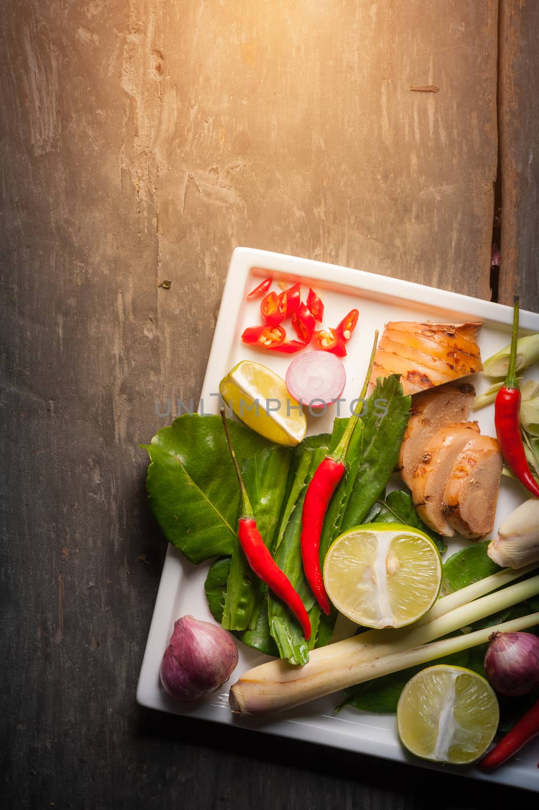 Ingredients set for Thai spicy soup (Tom-yum) include lemon, galangal, red chili, red onion, lemongrass, and kaffir lime leaf on wood table in morning scene