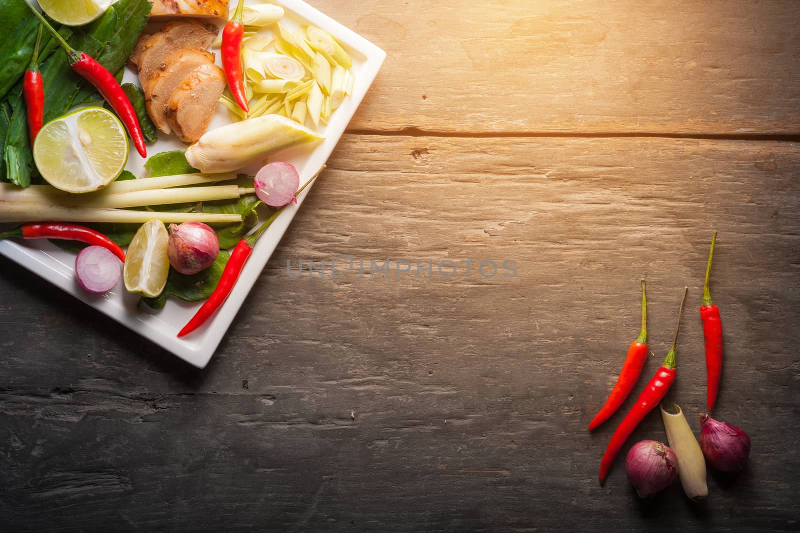 Ingredients set for Thai spicy soup (Tom-yum) include lemon, galangal, red chili, red onion, lemongrass, and kaffir lime leaf on wood table in low key morning scene with blank copyspace area for text or message
