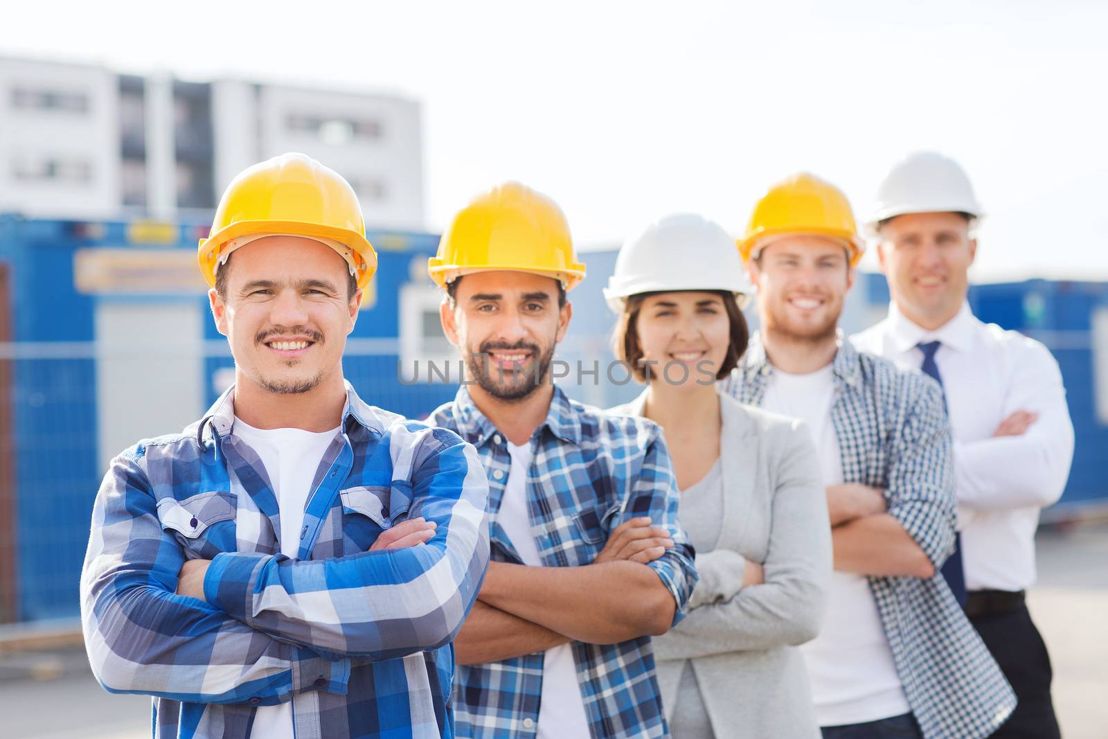 group of smiling builders in hardhats outdoors by dolgachov