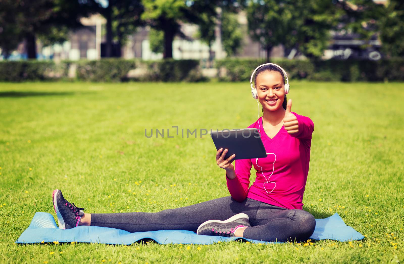 fitness, park, technology and sport concept - smiling african american woman with tablet pc and headphones showing thumbs up outdoors