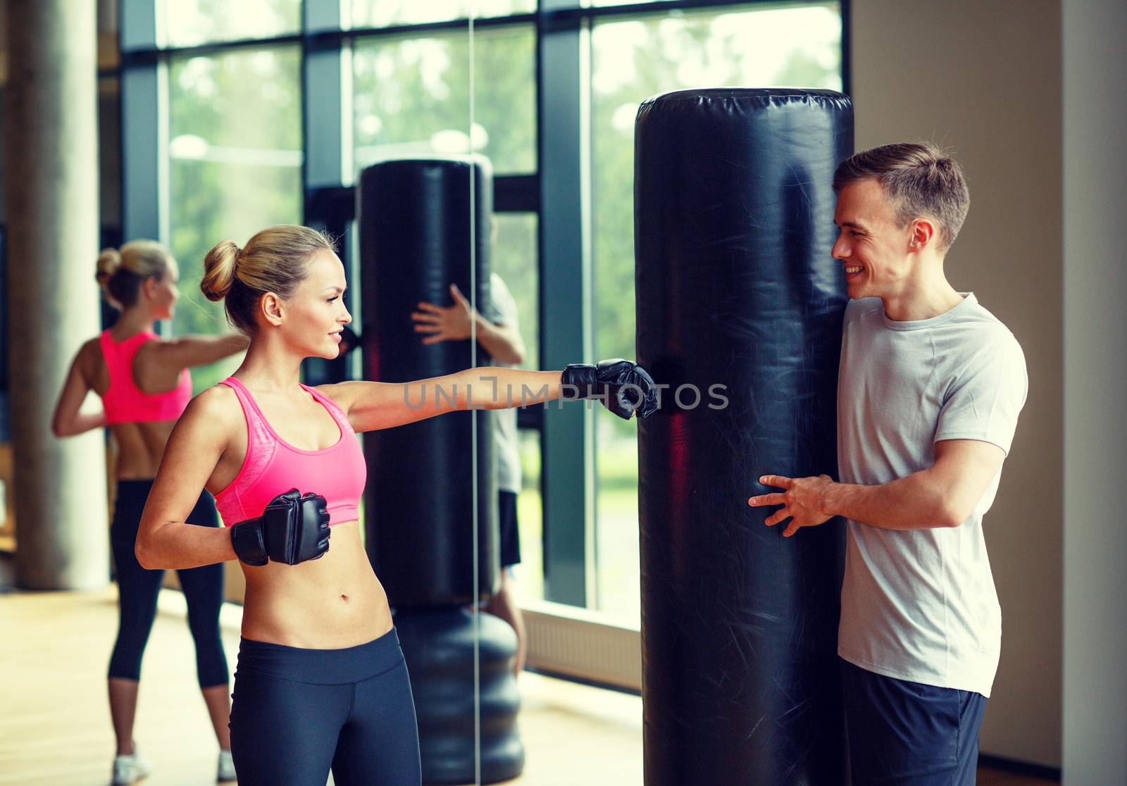 smiling woman with personal trainer boxing in gym by dolgachov