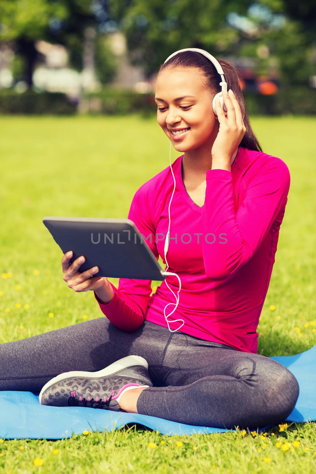 fitness, park, technology and sport concept - smiling african american woman with tablet pc computer and headphones on mat outdoors