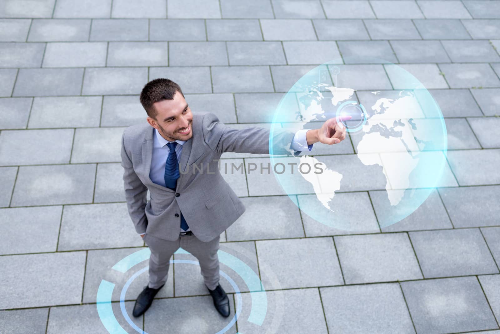 global business, development, technology and people and concept - young smiling businessman pointing finger to virtual globe projection outdoors from top