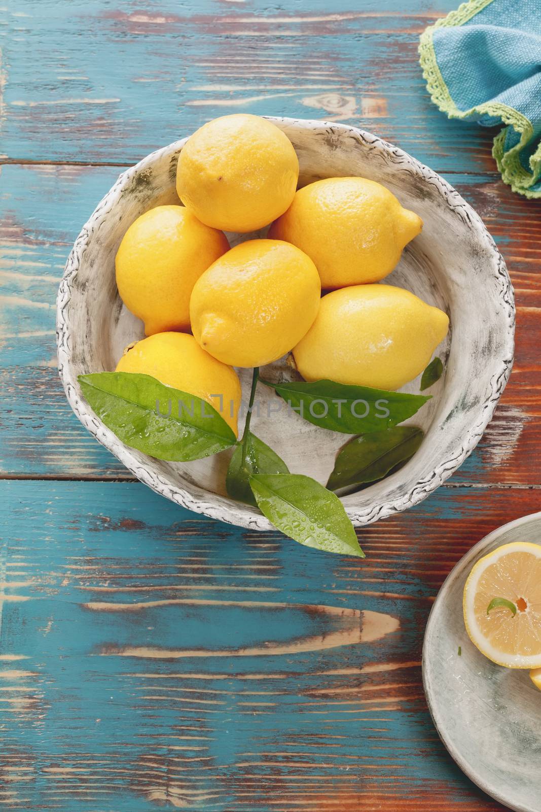 Fresh lemons with leaves in rustic ceramic bowl over wooden background. Macro, selective focus, vintage style. Natural light