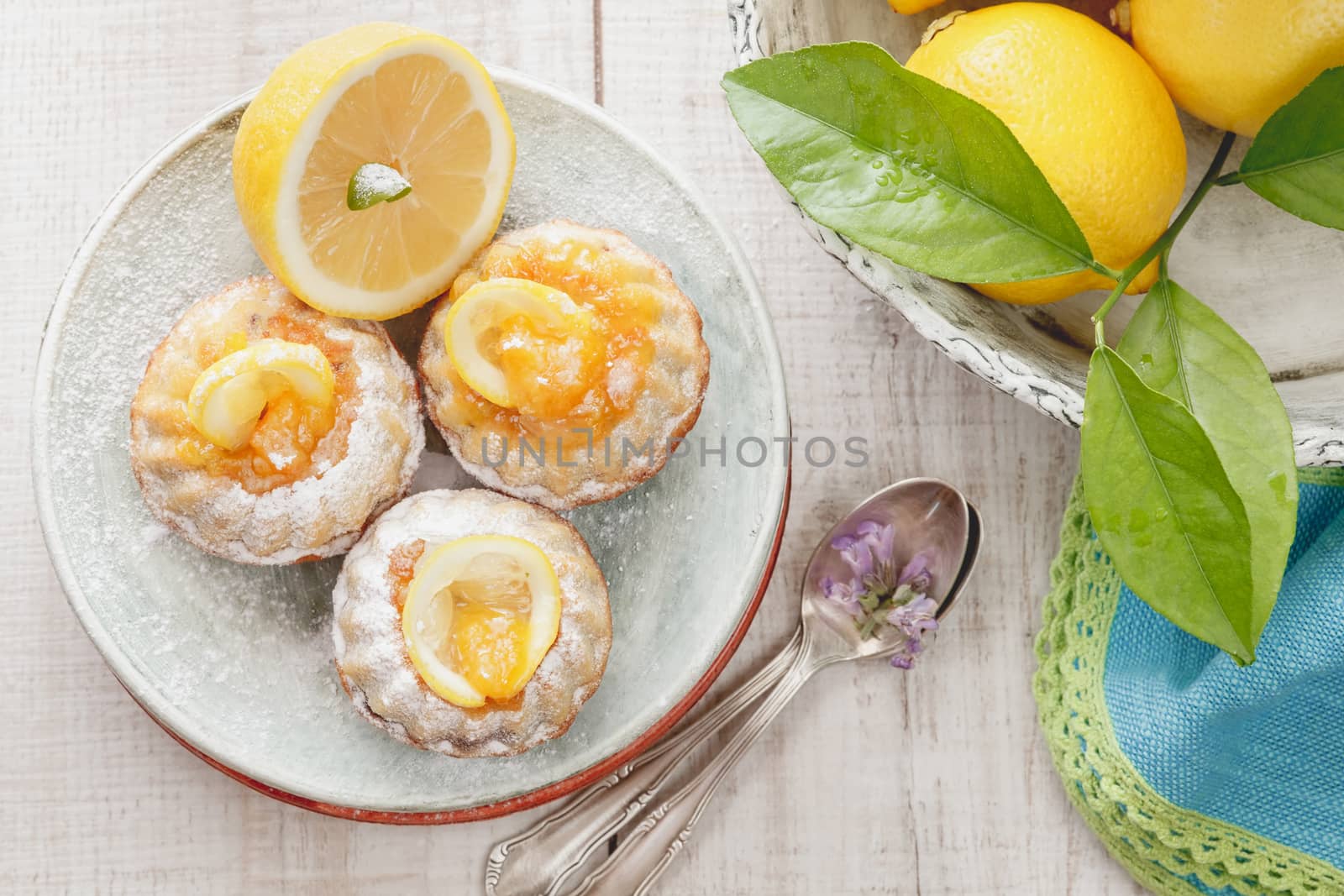 Mini lemon bundt cakes dusted with icing sugar and fresh lemons over rustic wooden background. Macro, selective focus. Natural light