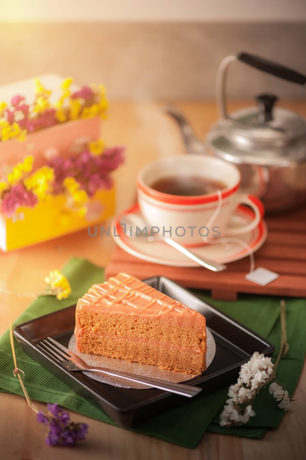 A piece of Thai tea cake on black ceramic dish with a cup of hot tea in background with morning scene