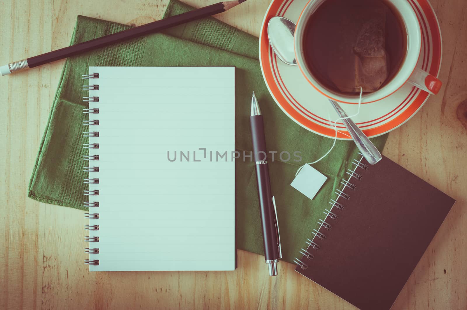 Opened notepad with pen and a cup of hot tea on wood table in cafe with film filter effect