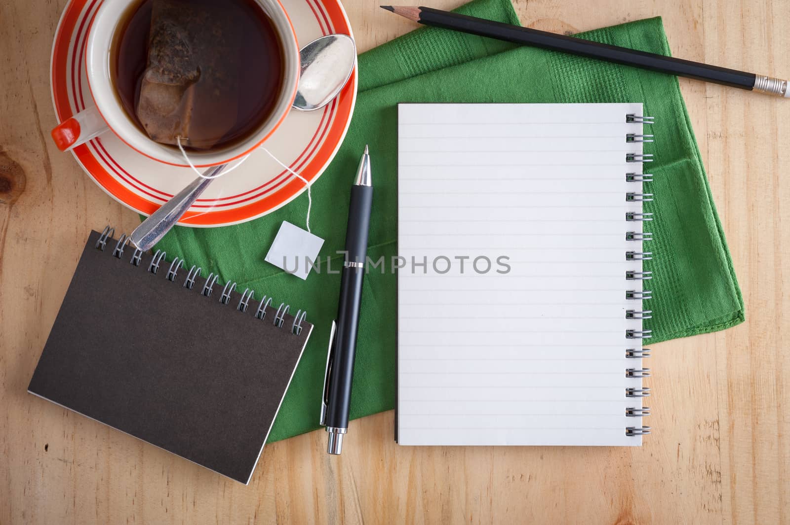 Opened notepad with pen and a cup of hot tea on wood table in cafe with morning scene