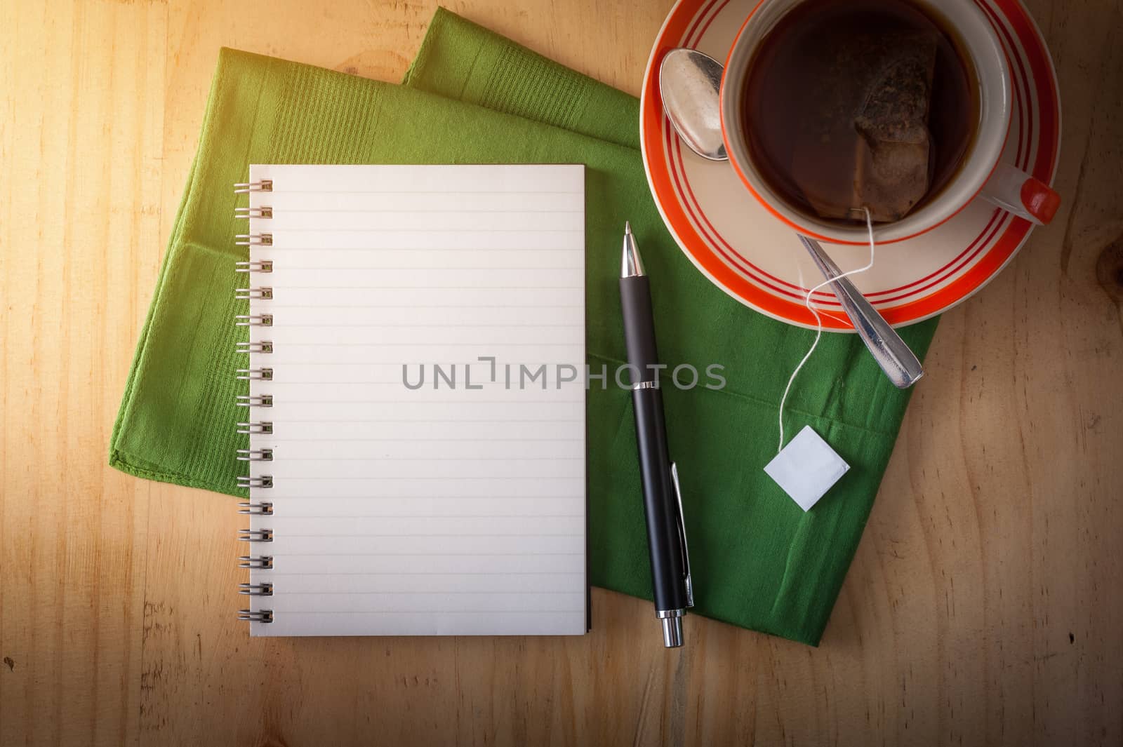 Opened notepad with pen and a cup of hot tea on wood table in cafe with morning scene