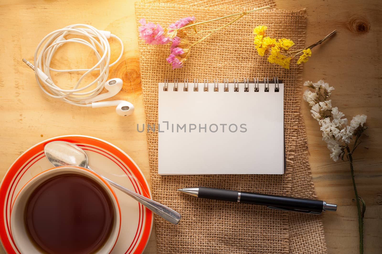 Opened notepad with pen, small earphone, and a cup of hot tea on wood table in cafe with morning scene