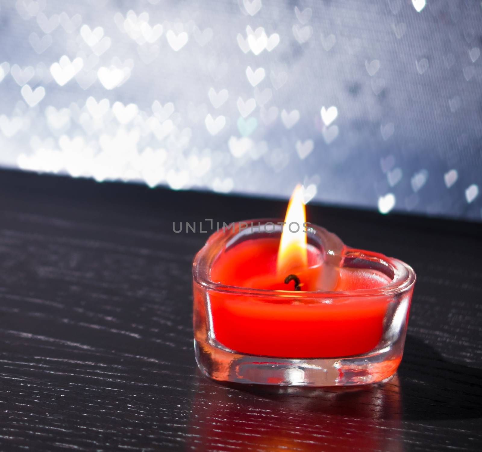 red burning heart shaped candle on silver hearts bokeh by donfiore