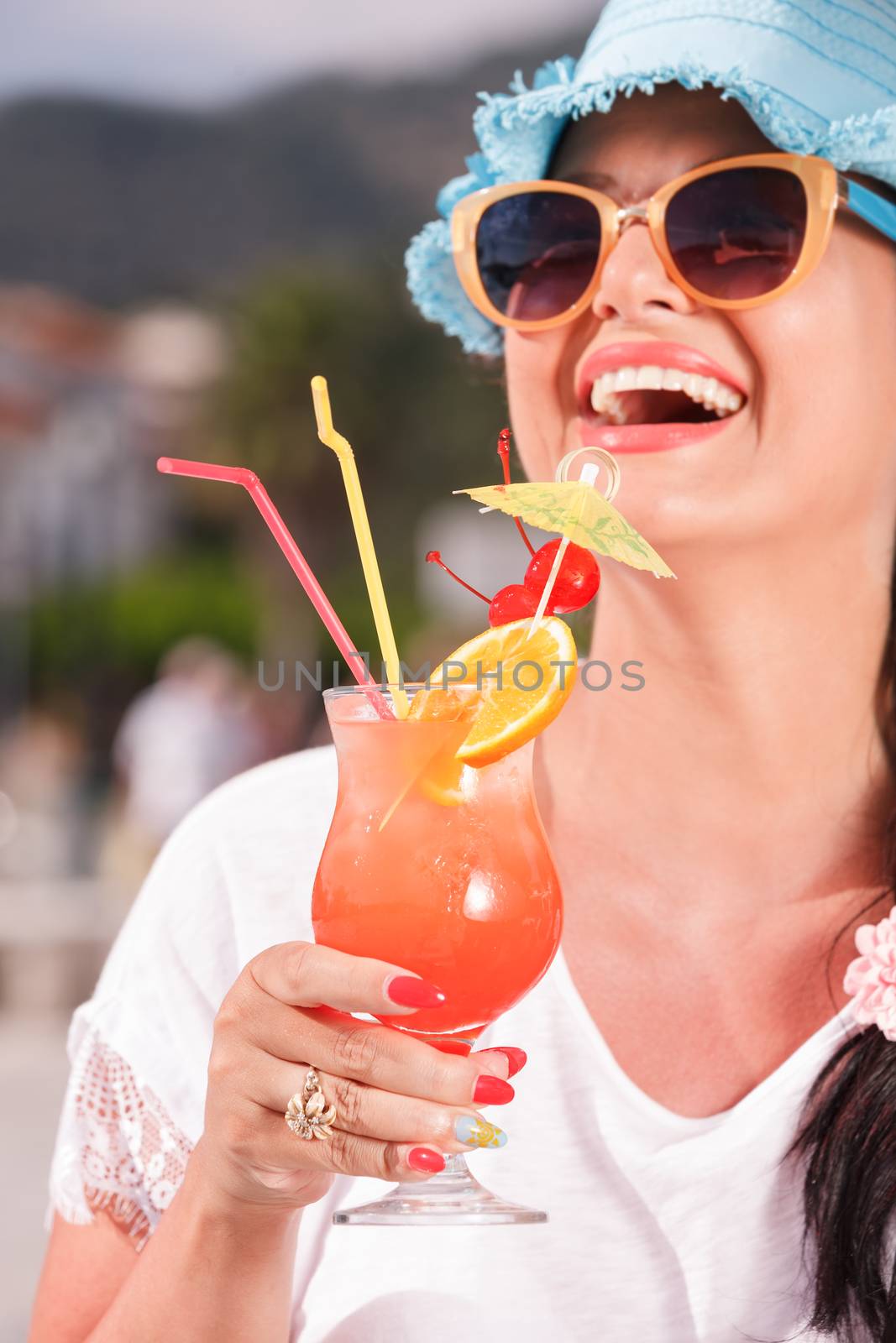 Happy young woman holding a glass of cocktail near the yacht marine. Shallow DOF with focus on the cocktail