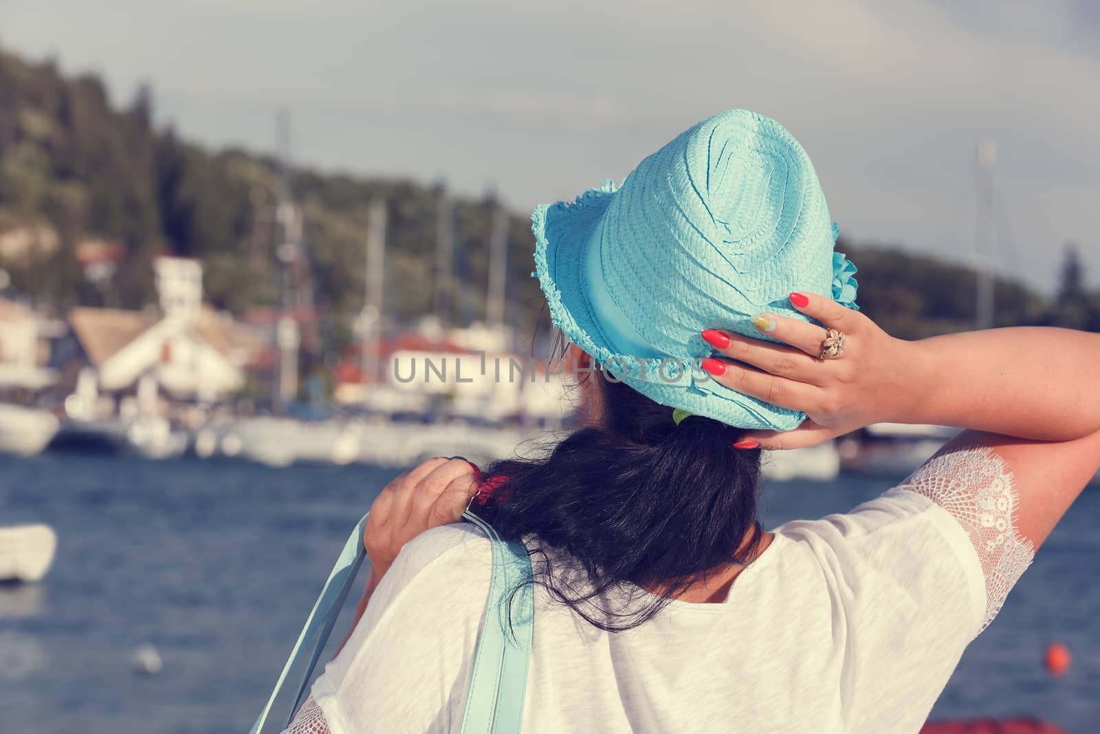 Back view of a woman wearing a straw hat looking at the sea, near the yacht marine