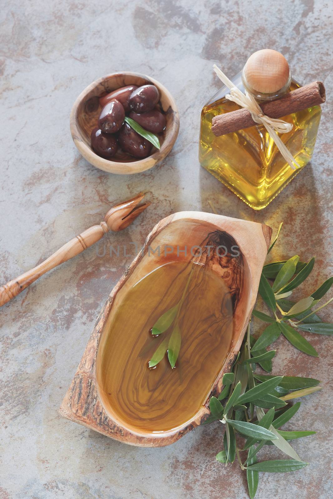 Olive oil in bowl and bottle, olive sprig beside it and black olives. Macro, selective focus, top view