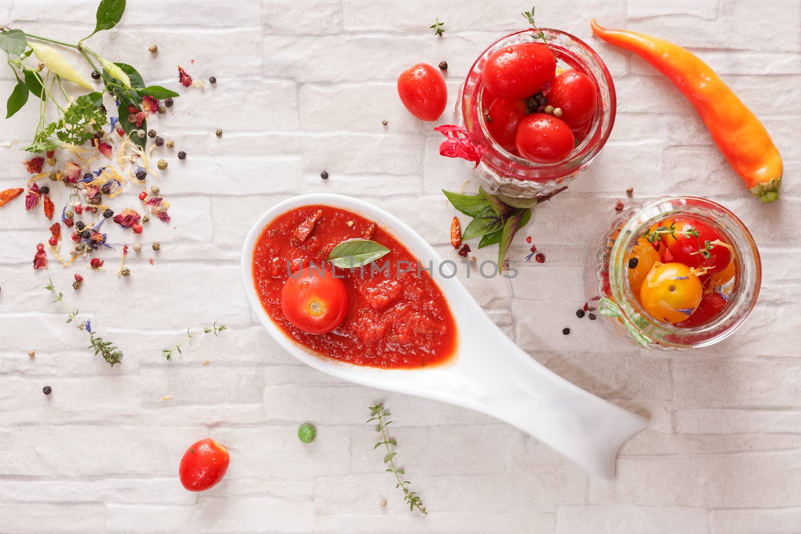 Spicy tomato jam on spoon and fresh tomatoes in a glass jar, top view