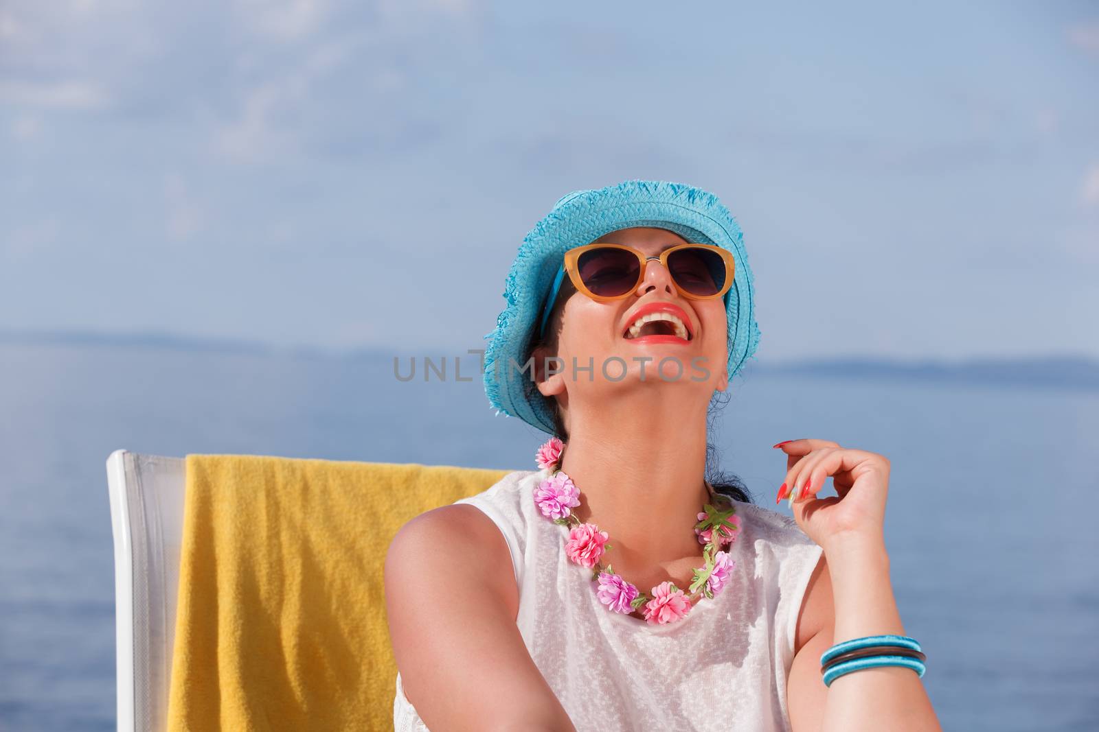 Happy woman with straw hat sitting on lounge chair at the beach and enjoying her beach vacation