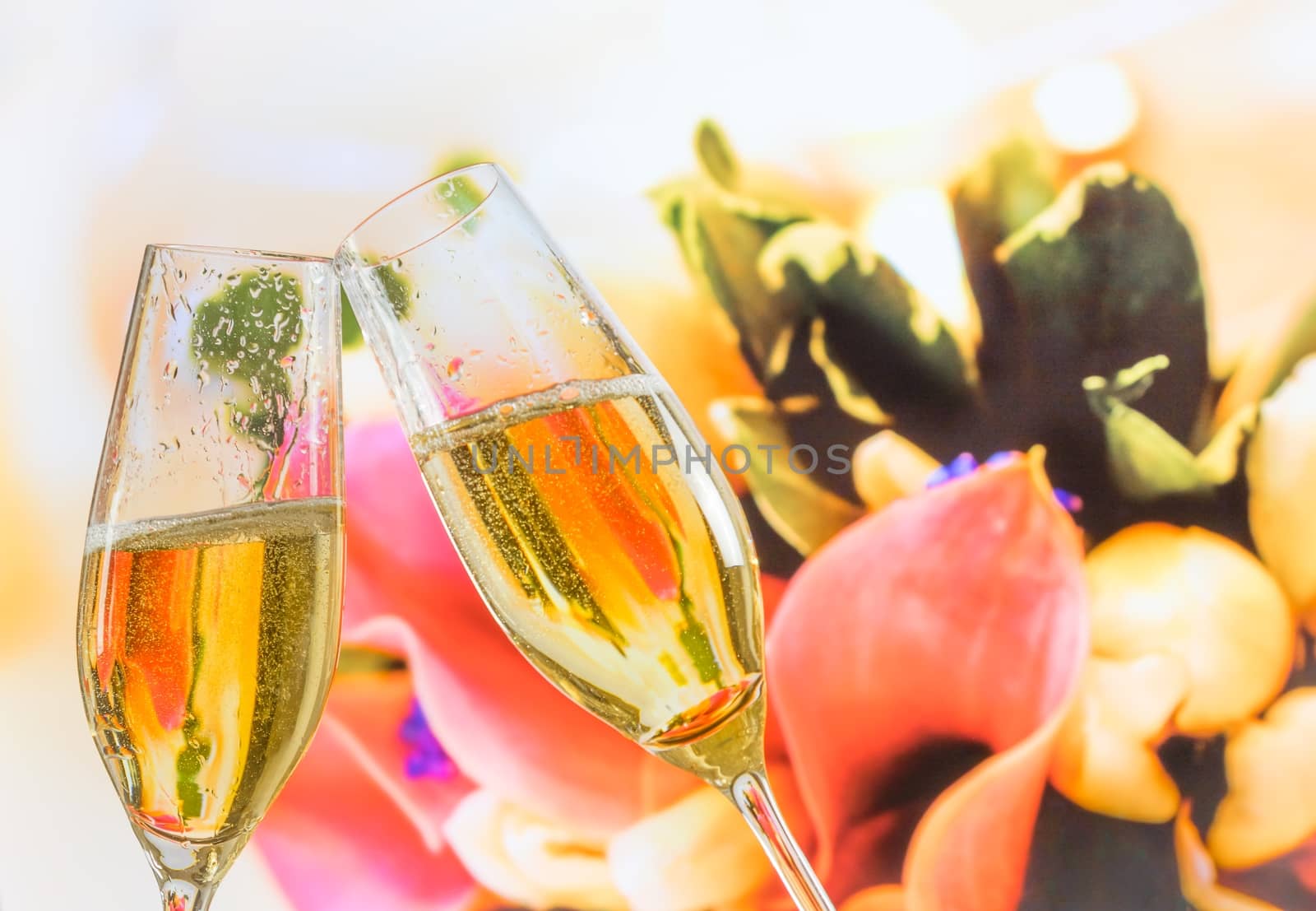champagne flutes with golden bubbles on wedding flowers background by donfiore
