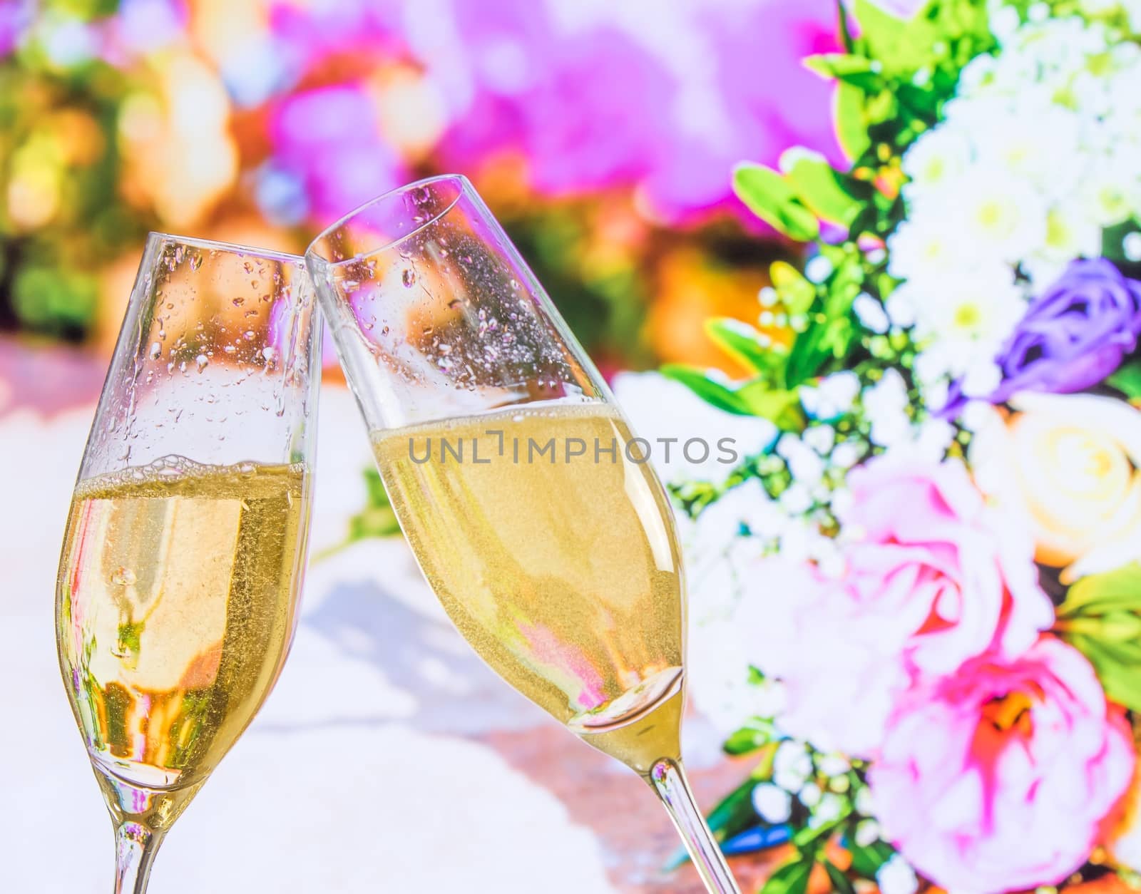 champagne flutes with golden bubbles on wedding flowers background by donfiore