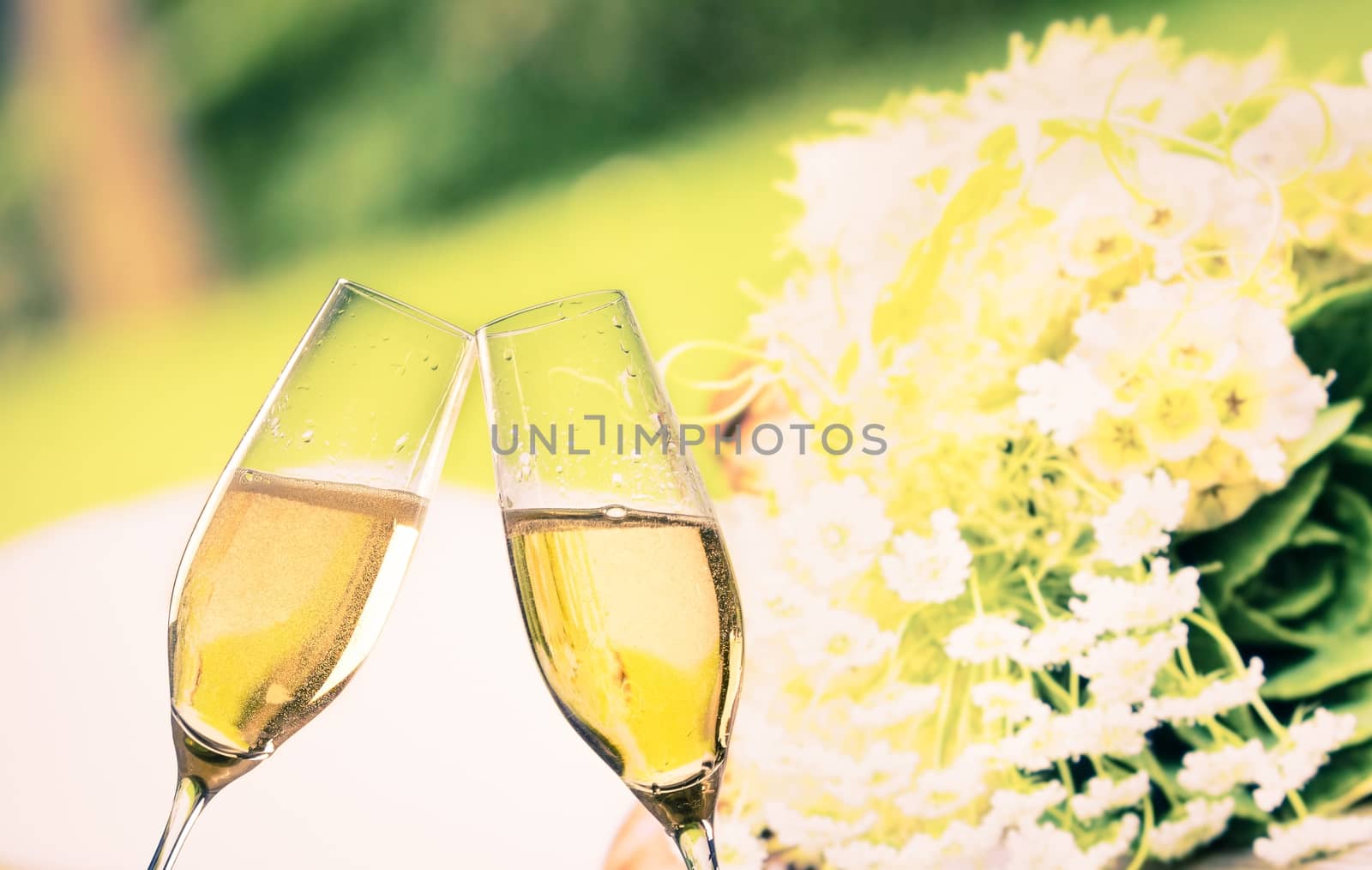 champagne flutes with golden bubbles make cheers on wedding flowers background
