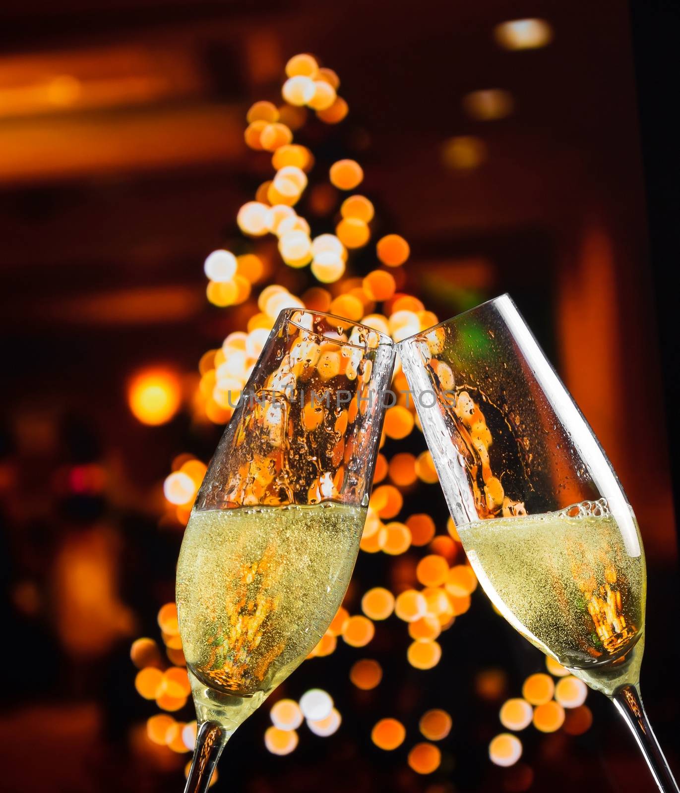 champagne flutes with golden bubbles on christmas lights decoration background by donfiore