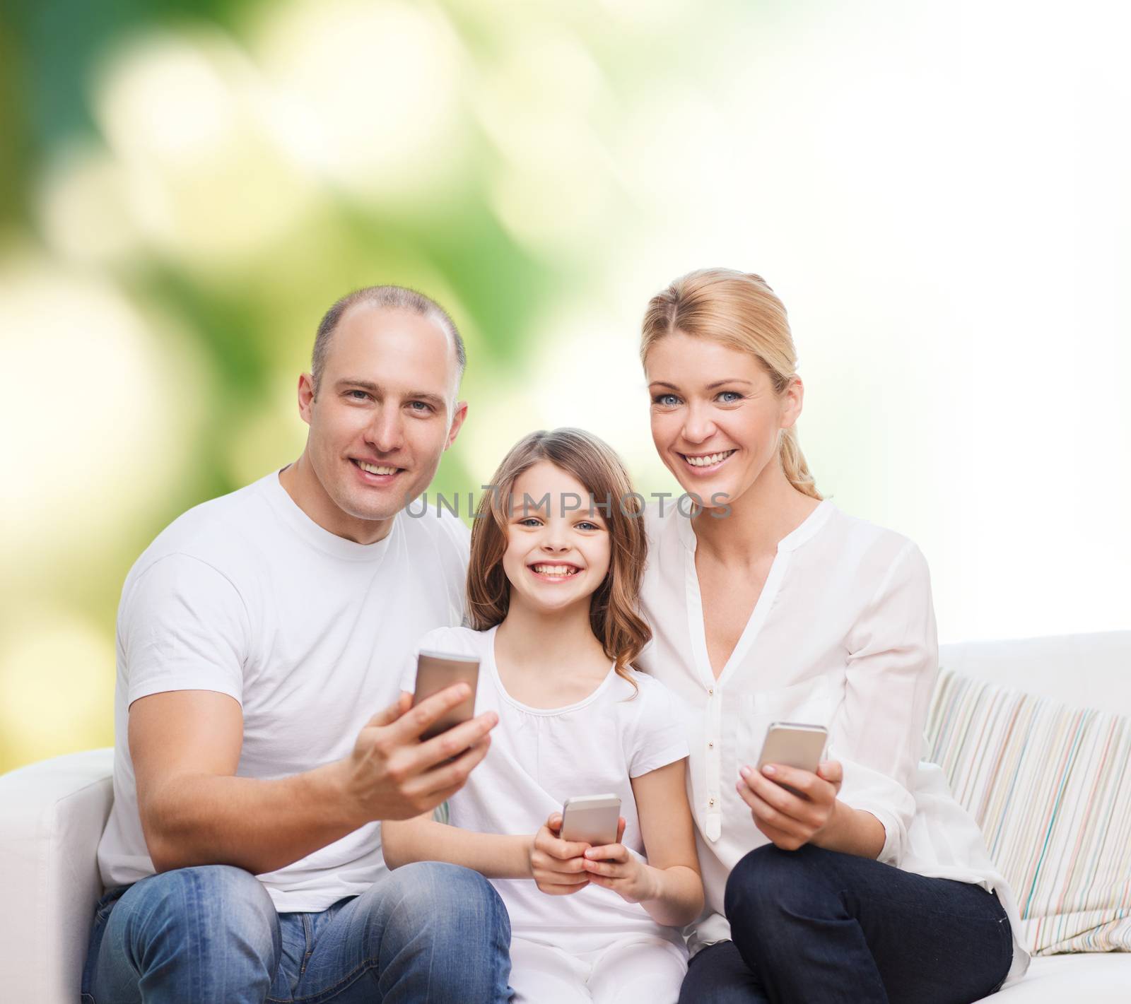 family, summer, technology and people concept - smiling mother, father and little girl with smartphones over green background