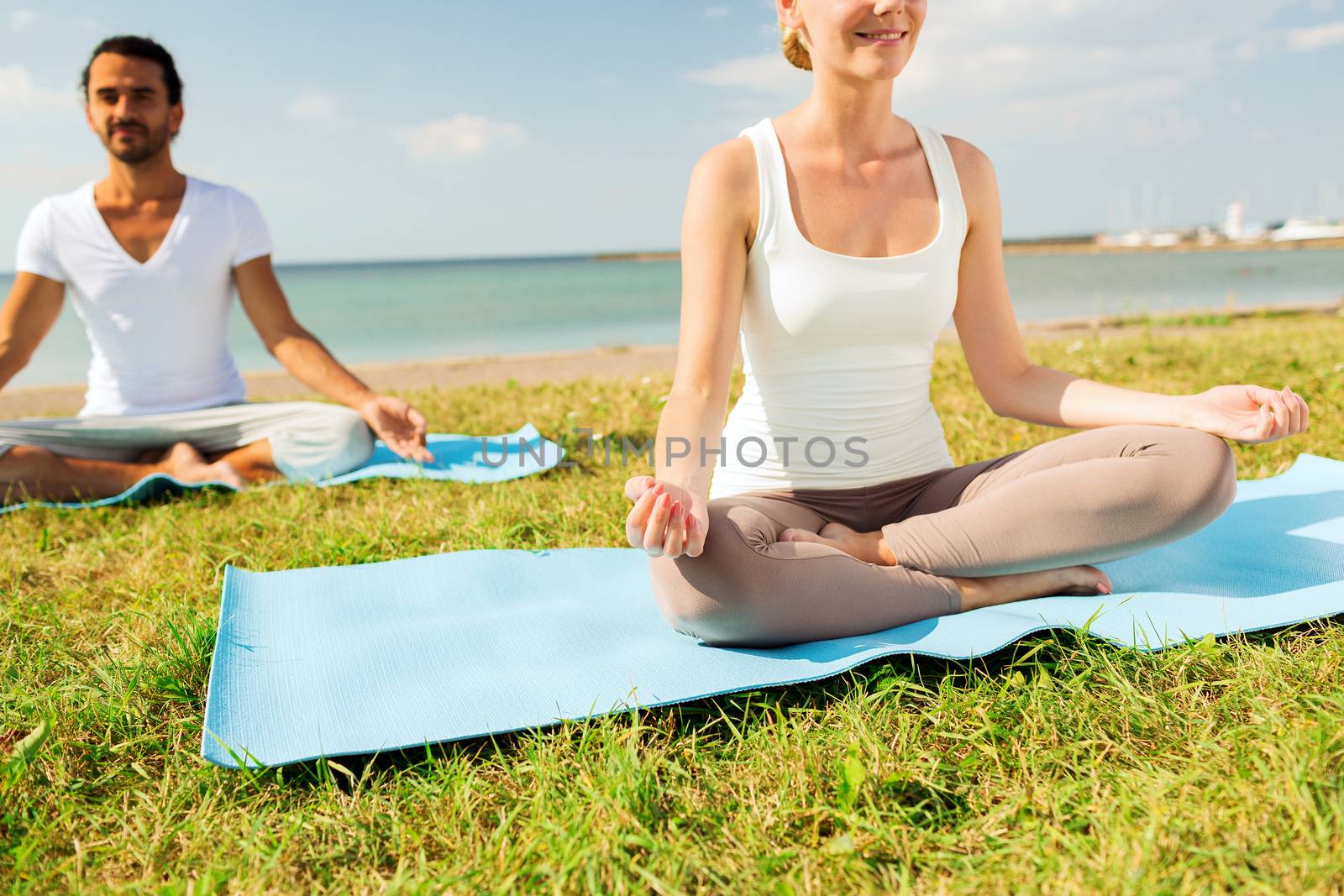 fitness, sport, people and lifestyle concept - close up of smiling couple making yoga exercises sitting on mats outdoors