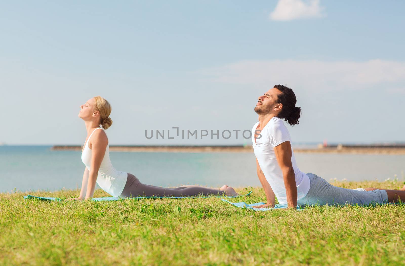 fitness, sport, friendship and lifestyle concept - smiling couple making yoga exercises lying on mats outdoors