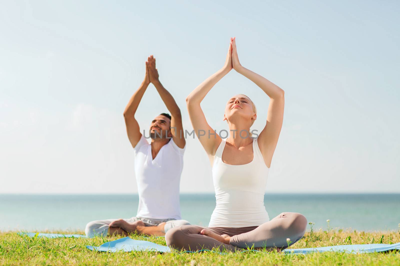 smiling couple making yoga exercises outdoors by dolgachov