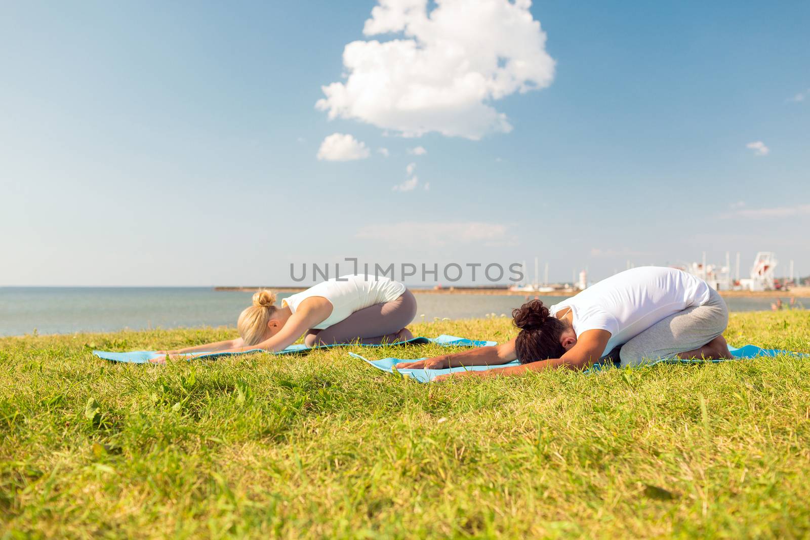 fitness, sport, people and lifestyle concept - couple making yoga exercises on mats outdoors