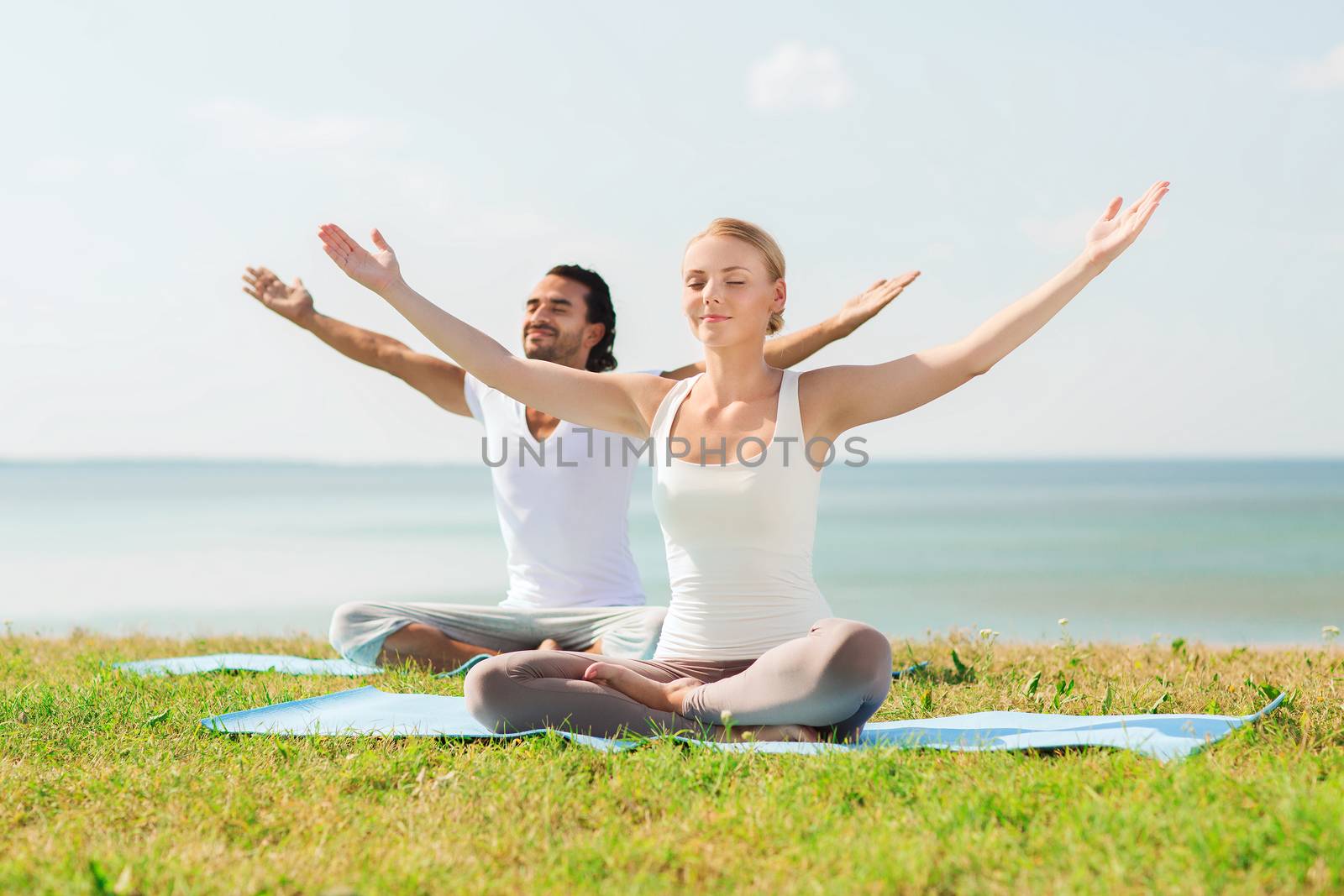 smiling couple making yoga exercises outdoors by dolgachov