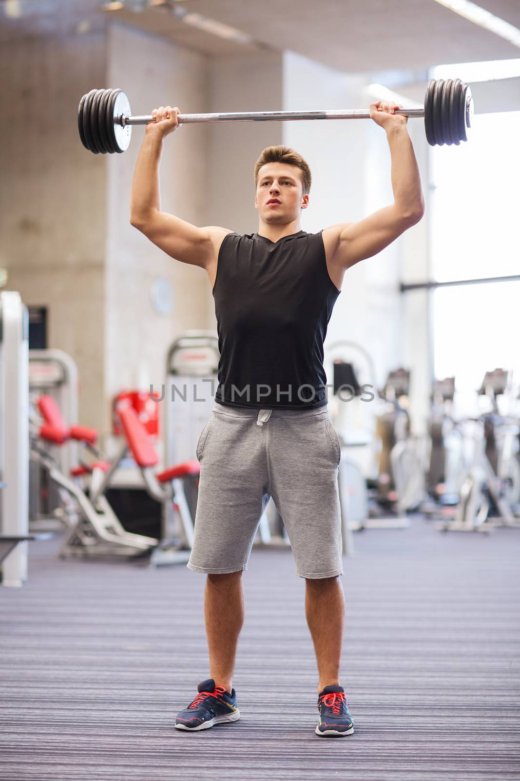 young man flexing muscles with barbell in gym by dolgachov