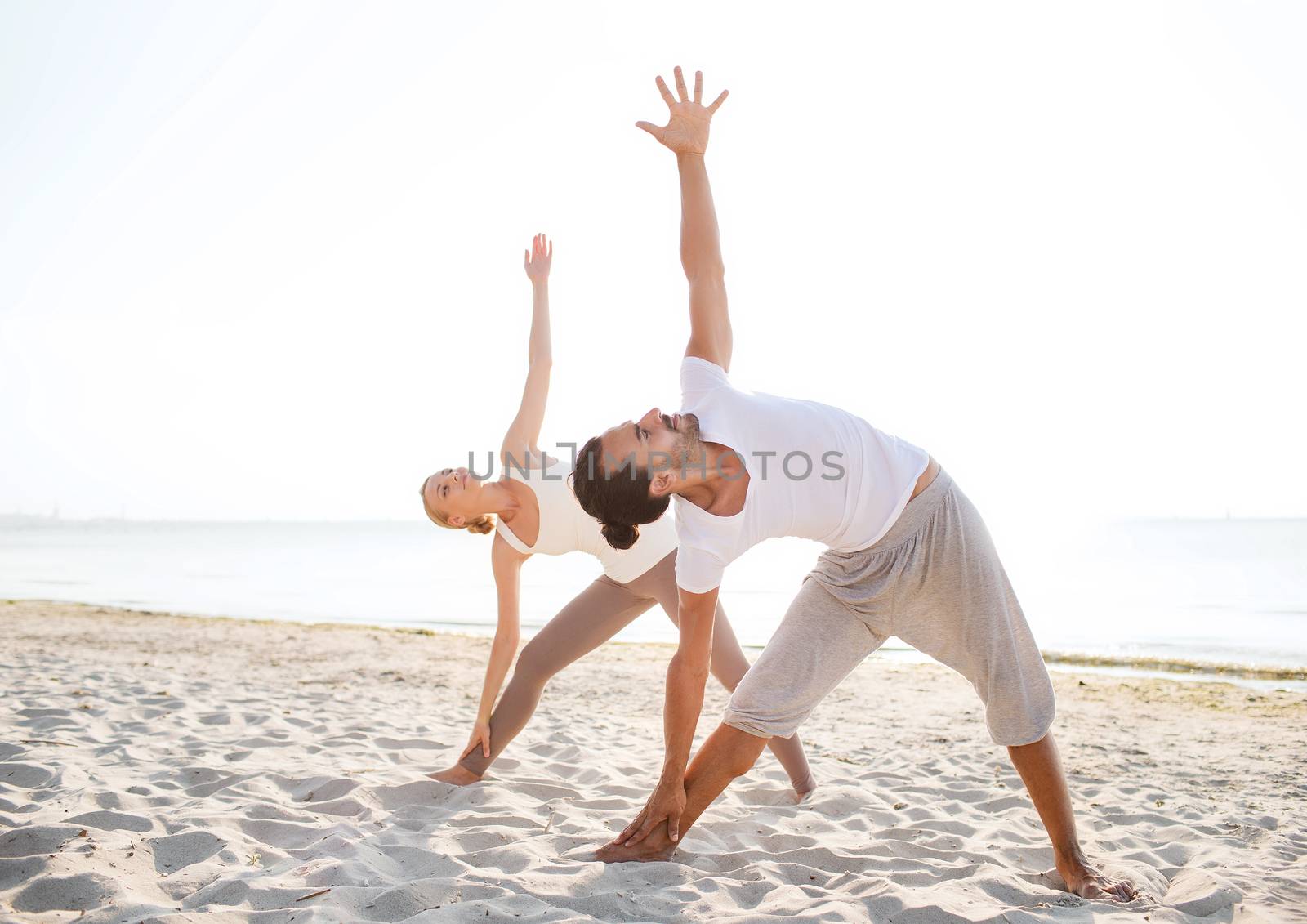 fitness, sport, friendship and lifestyle concept - couple making yoga exercises on beach