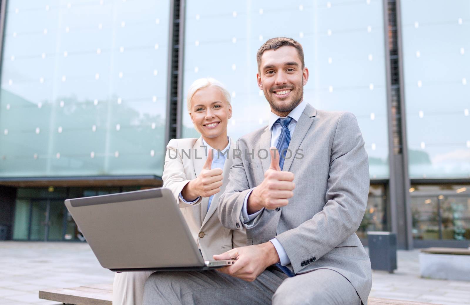 business, education, technology, gesture and people concept - smiling businesspeople working with laptop computer showing thumbs up on city street