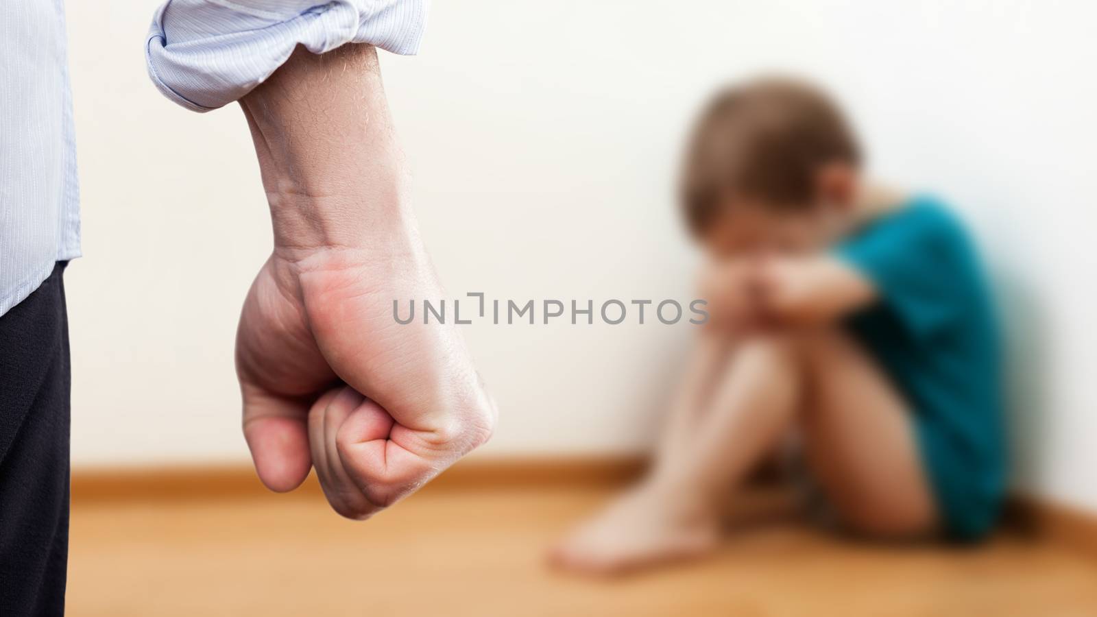 Family violence and aggression concept - furious angry man raised punishment fist over scared or terrified child boy sitting at wall corner