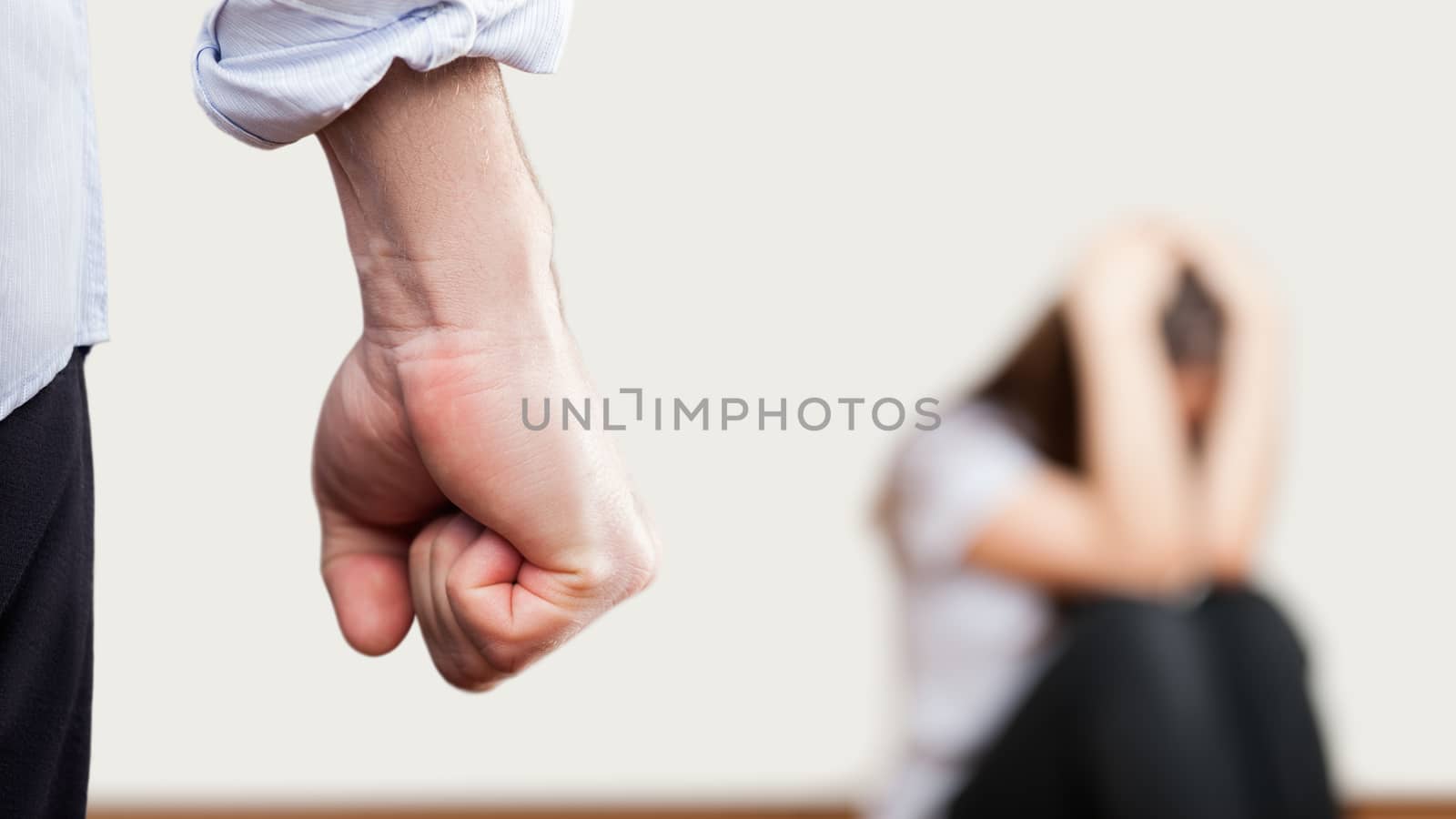 Family violence and aggression concept - furious angry man raised punishment fist over scared or terrified woman sitting at wall corner