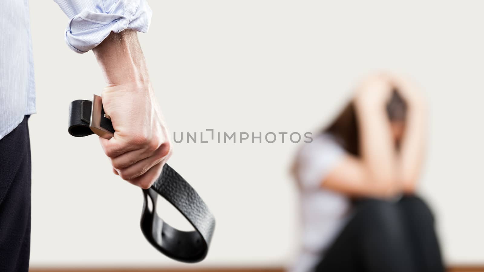 Angry man raised hand holding leather belt over wall corner sitting woman by ia_64