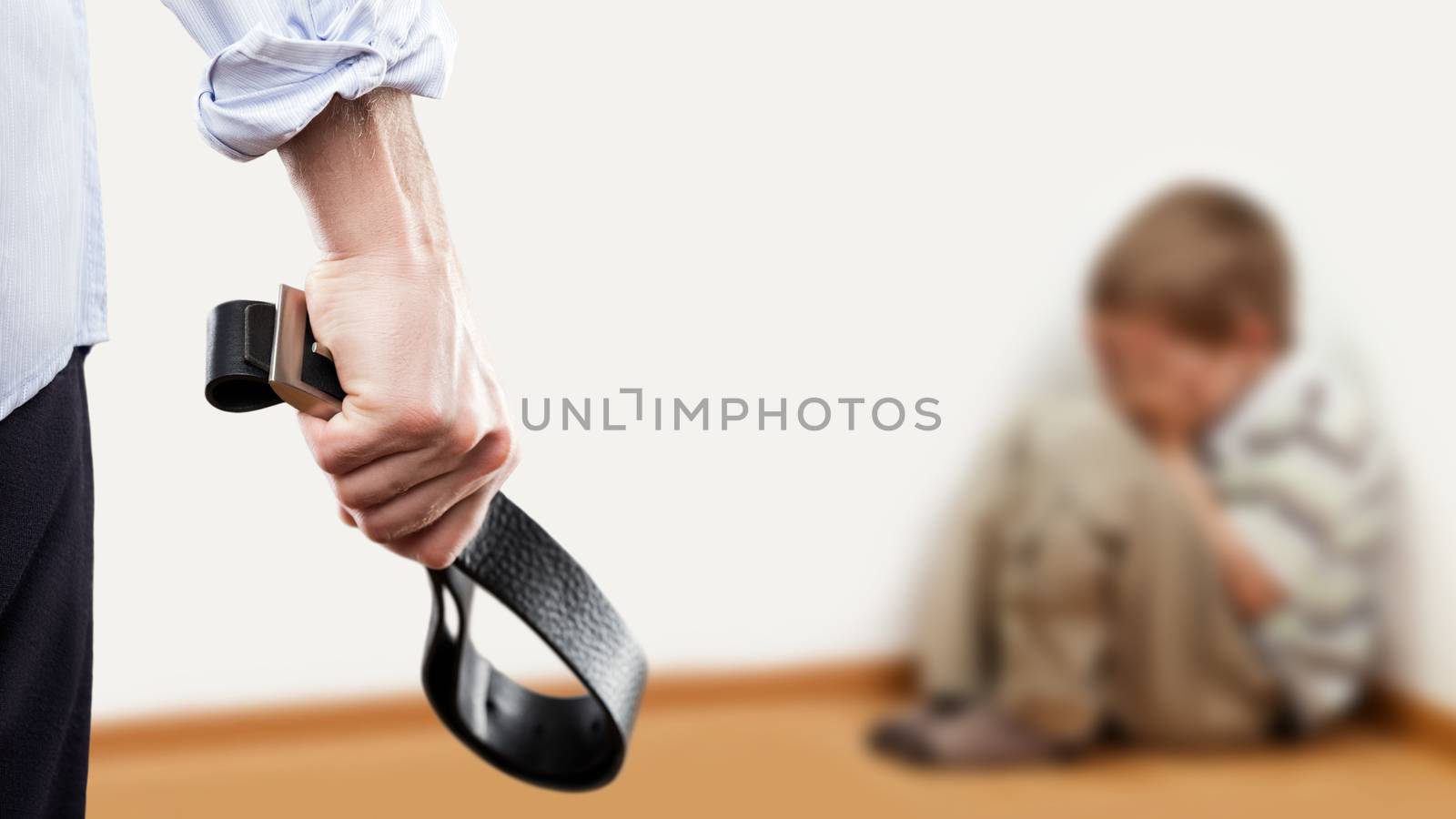 Family violence and aggression concept - furious angry man raised punishment hand holding leather belt over scared or terrified child boy sitting at wall corner