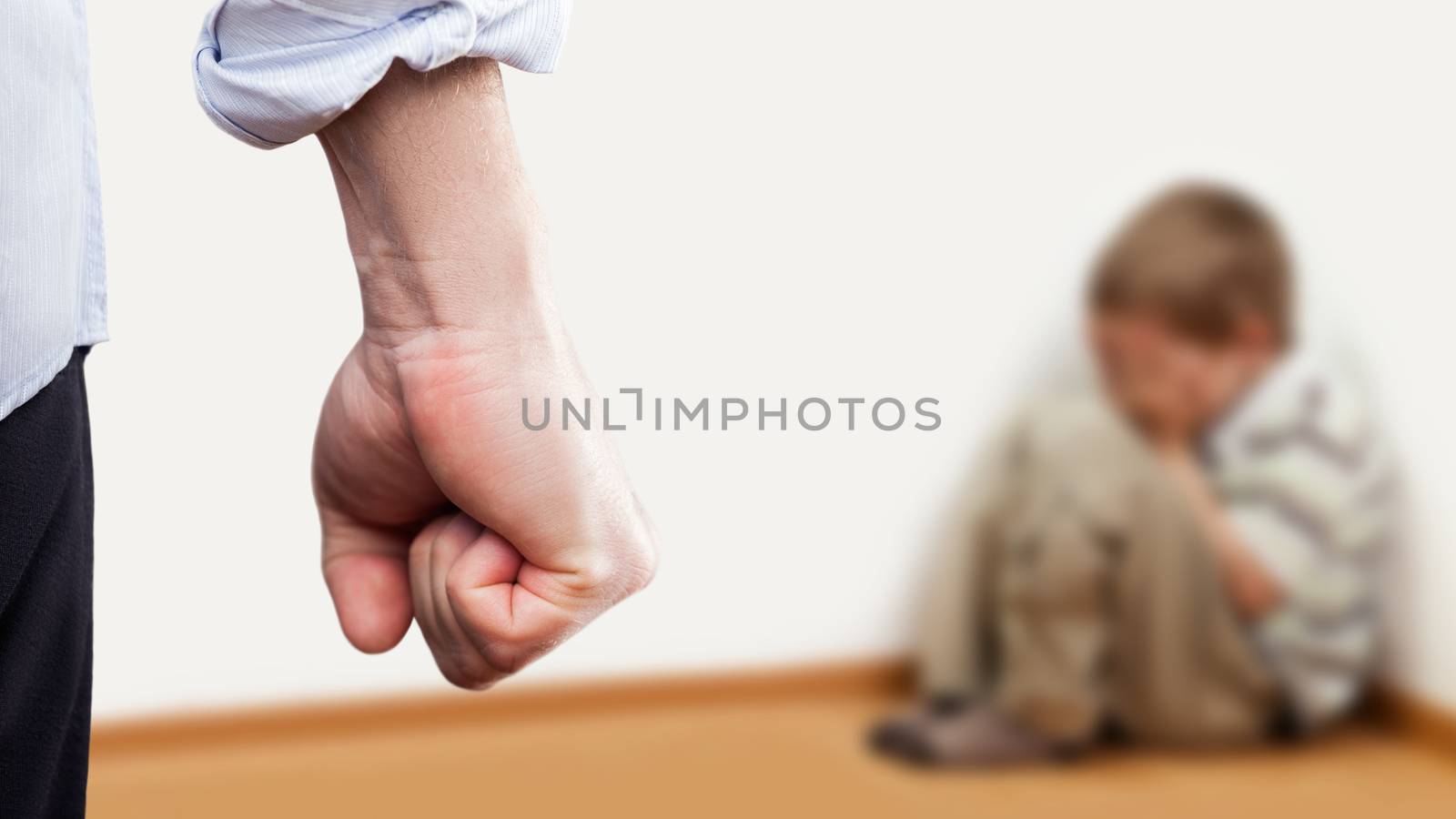 Family violence and aggression concept - furious angry man raised punishment fist over scared or terrified child boy sitting at wall corner