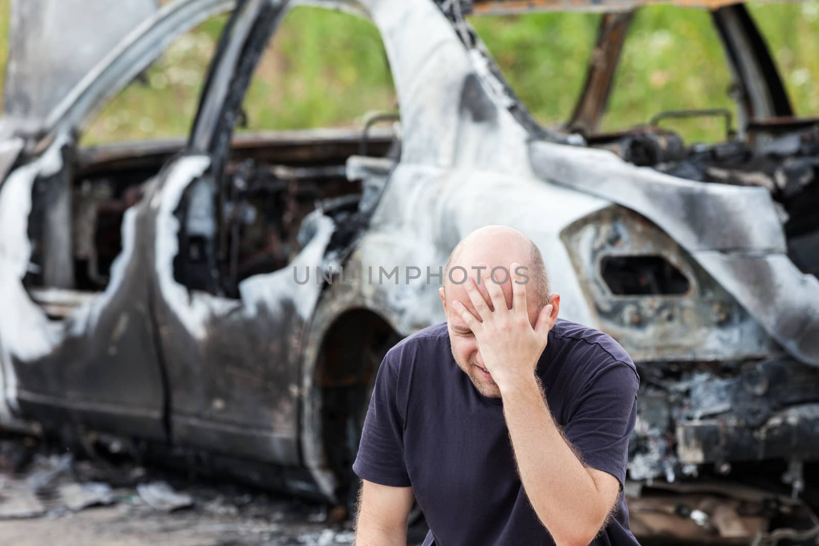Crying upset caucasian man at road wreck accident or arson fire burnt wheel car vehicle junk