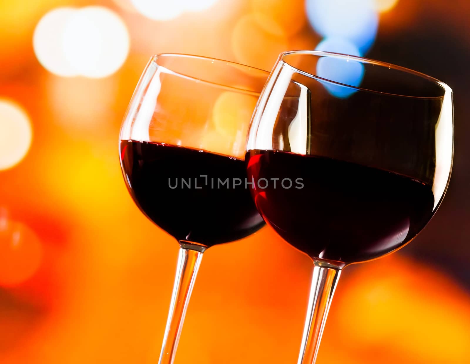 two red wine glasses against colorful bokeh lights background by donfiore