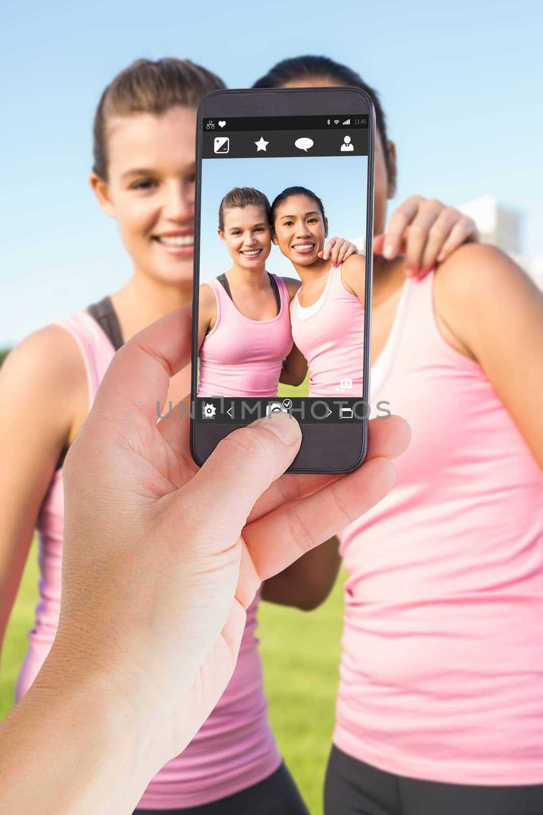 Female hand holding a smartphone against two smiling women wearing pink for breast cancer