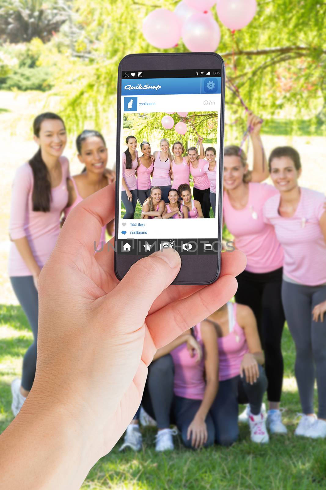 Female hand holding a smartphone against smiling women in pink for breast cancer awareness