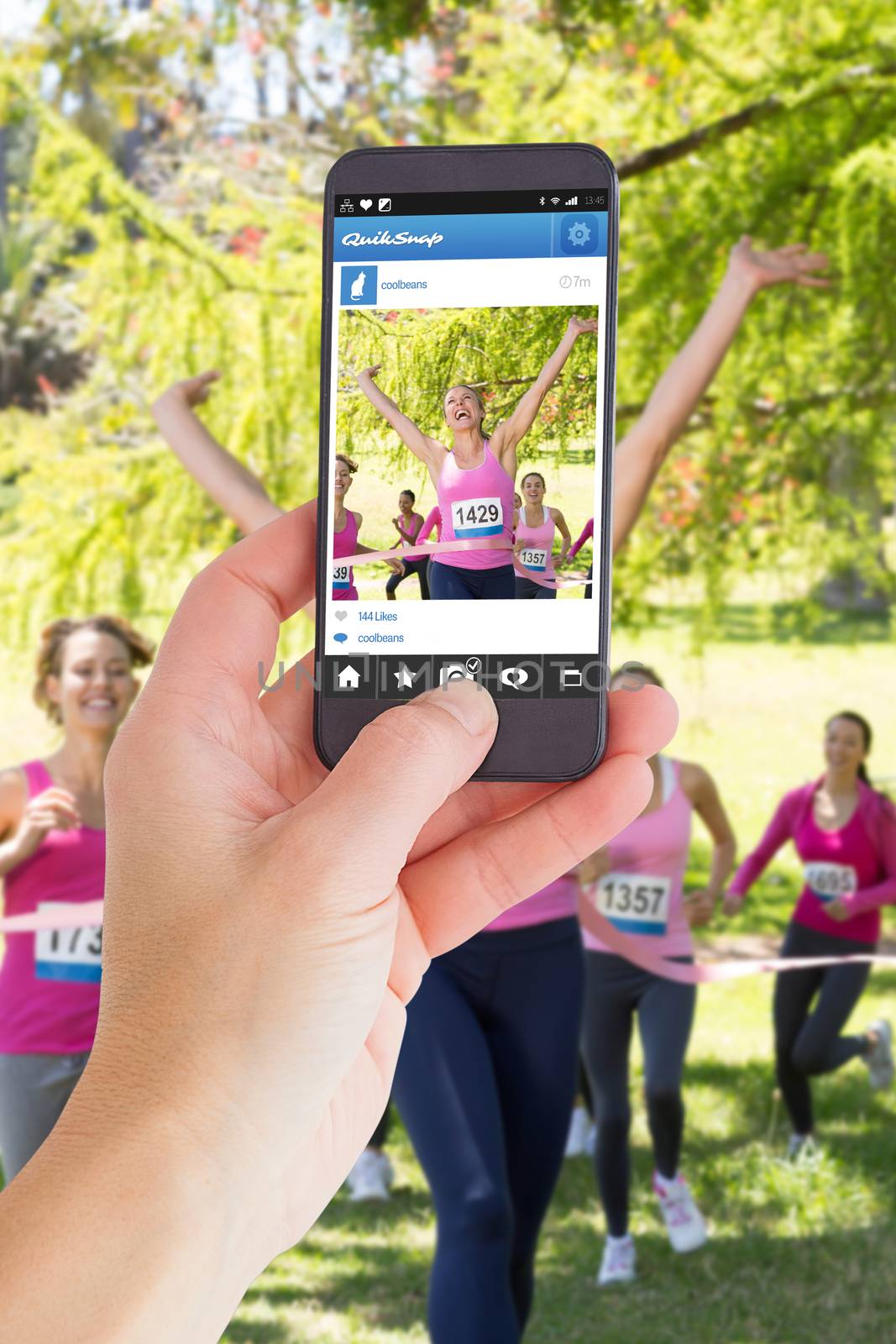 Female hand holding a smartphone against smiling women running for breast cancer awareness