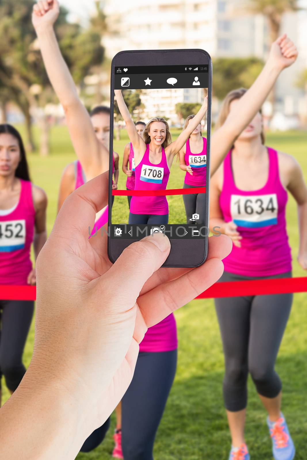 Female hand holding a smartphone against cheering blonde winning breast cancer marathon