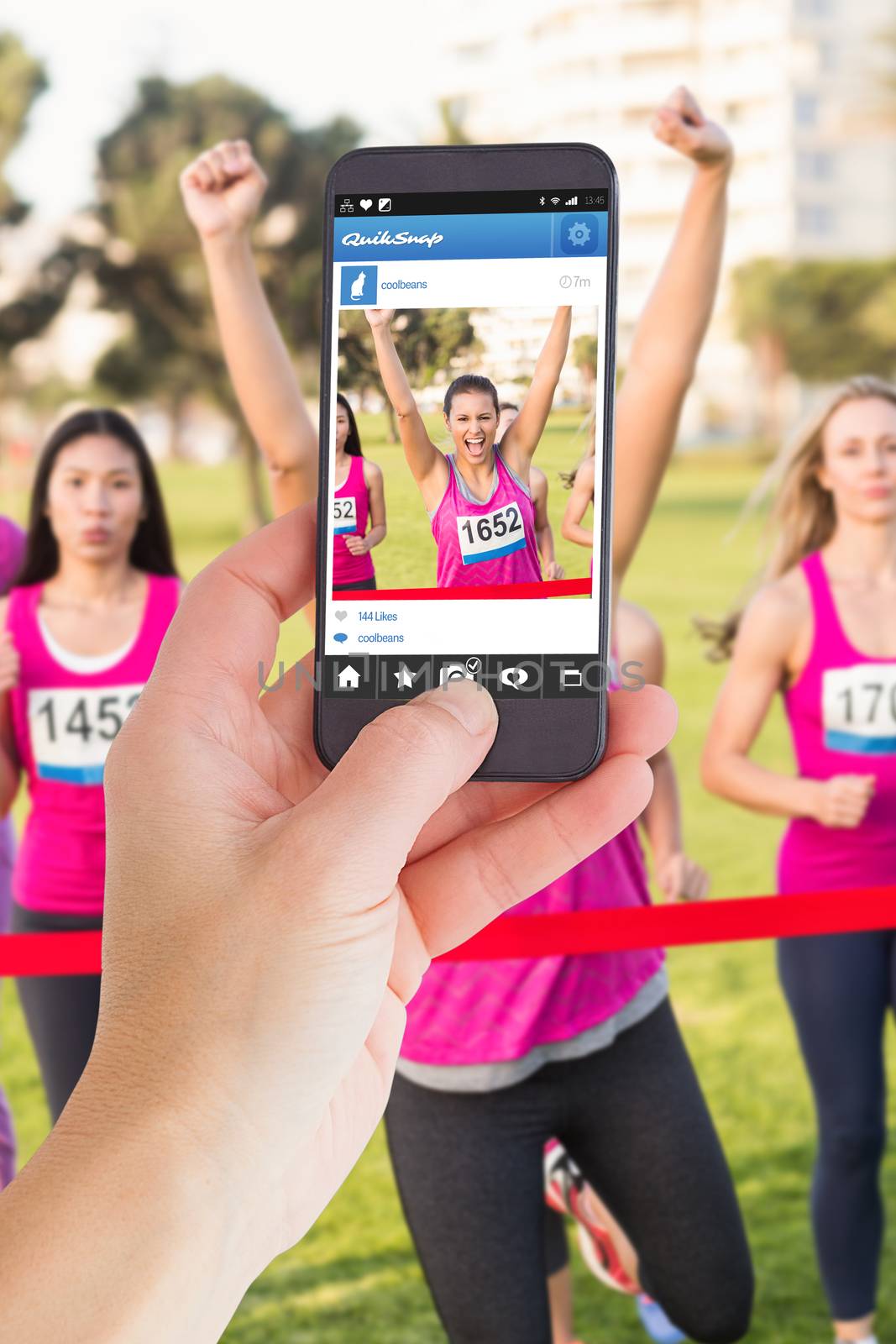 Female hand holding a smartphone against cheering brunette winning breast cancer marathon