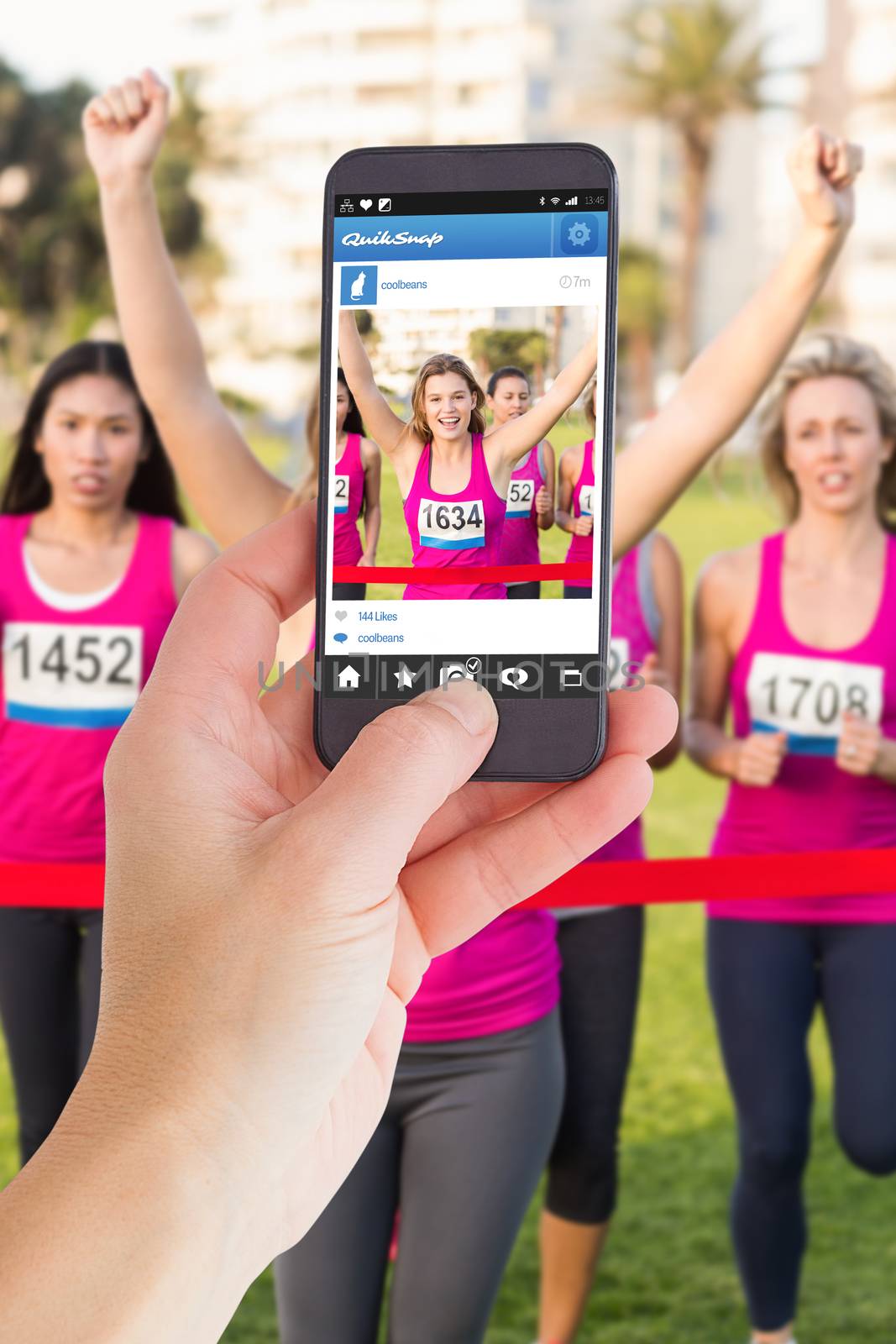 Female hand holding a smartphone against cheering blonde winning breast cancer marathon