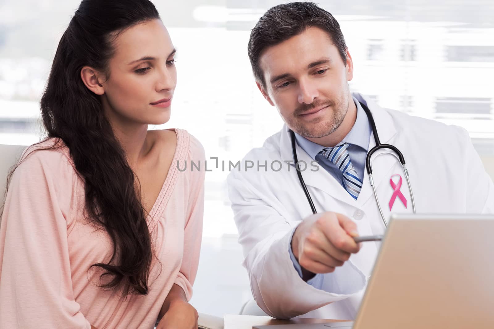 Pink awareness ribbon against male doctor showing something on laptop to patient