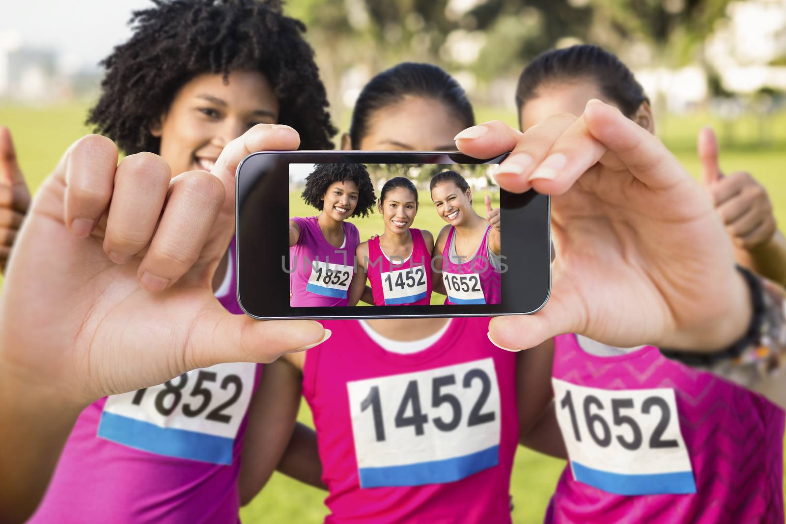 Hand holding smartphone showing against three smiling runners supporting breast cancer marathon 