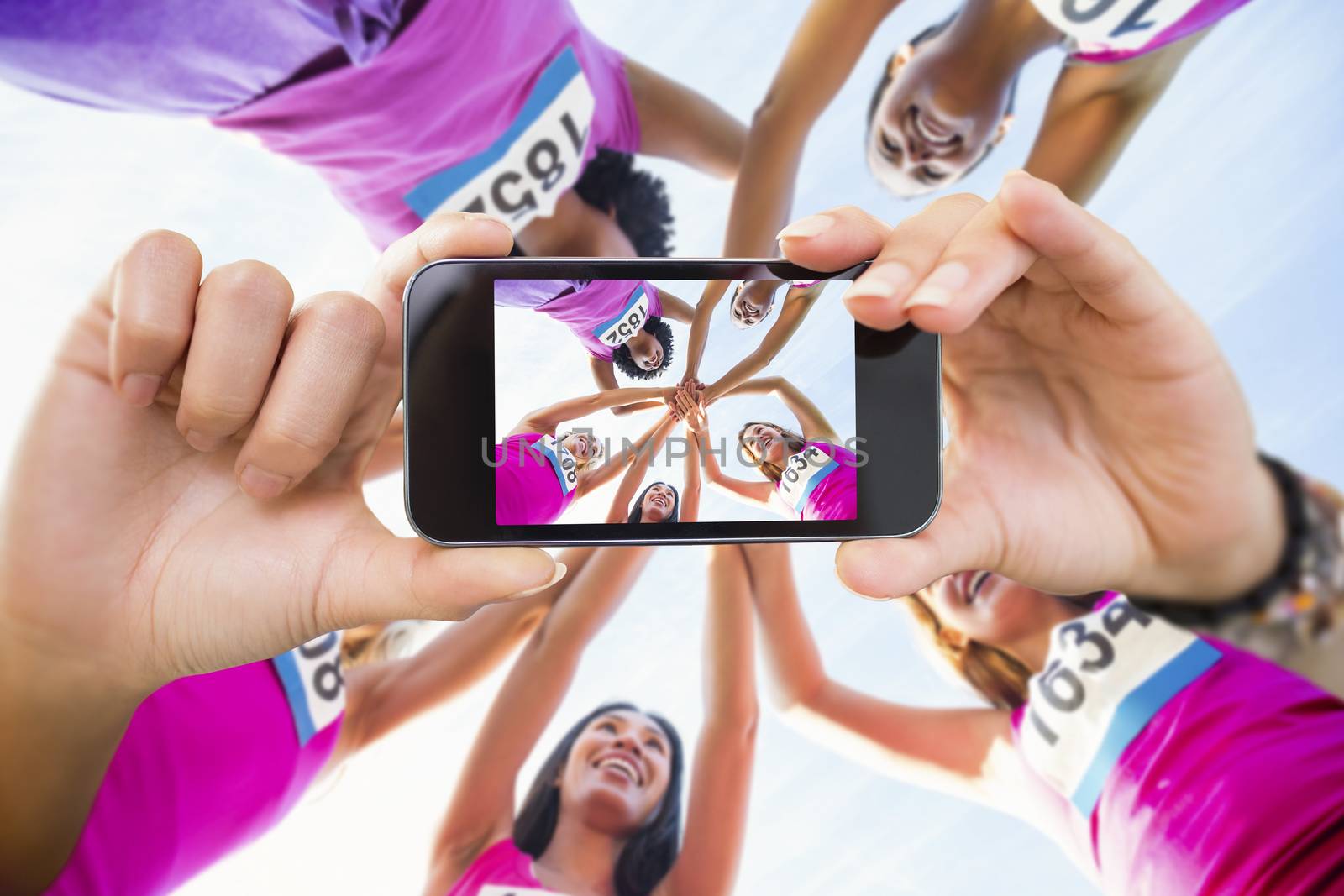 Hand holding smartphone showing against five smiling runners supporting breast cancer marathon